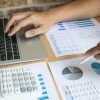 meno de persona en escritorio con notebook abierta, calculadora y hojas con balances